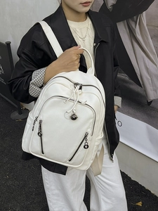 White pebbled leather backpack with orb logo worn by a model in a street style setting