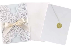 Detail of laser-cut white rose wedding invitation with silk bow and gold seal sticker