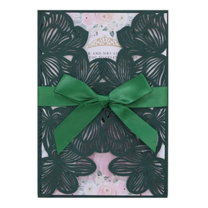 Detail of dark green laser cut floral wedding invitation with a satin ribbon bow