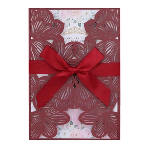 Detail of laser-cut burgundy wedding invitation featuring a floral pattern and velvet bow