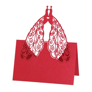 Close-up of red laser-cut peacock place card with intricate hollowed patterns and glittery finish