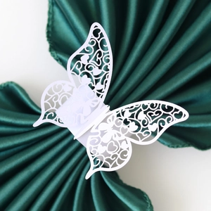 Detail showing white laser-cut butterfly napkin ring on a dark green satin fabric
