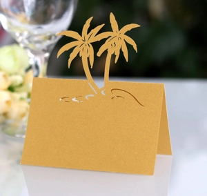 Macro detail of laser-cut coconut trees on a golden pearlescent paper wedding place card
