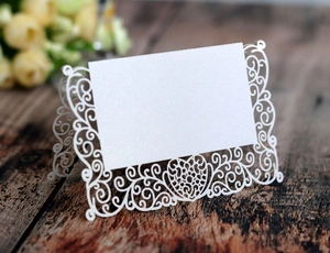 Detail view of laser-cut white pearl paper place cards with elegant scroll heart patterns