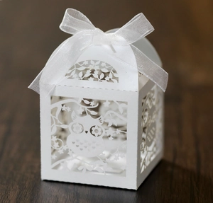 Elegant white laser-cut owl favor box with white ribbon bow on a rustic wood table
