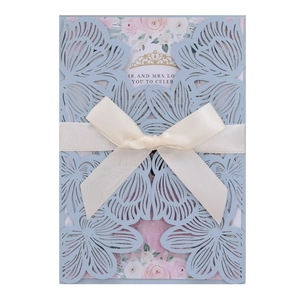 Detail of laser-cut blue floral wedding invitation with cream satin ribbon bow and gold crown