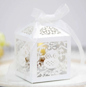 Close-up of hollow owl paper candy box with laser-cut floral patterns and a white silk ribbon