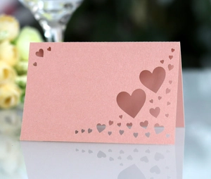 Macro shot of laser-cut heart pattern on pink pearlescent paper wedding place card