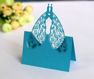 Detail of blue laser-cut peacock place card with intricate hollowed patterns on desk