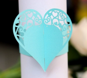 Macro detail of laser-cut heart napkin ring with intricate floral patterns in mint green