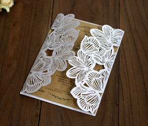 Close-up of laser-cut white floral invitation with kraft insert on dark wood background
