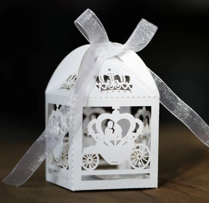Macro shot of laser-cut white wedding favor box with carriage design and crown top
