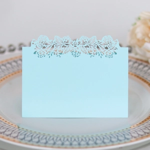 Detail of light blue laser-cut place card with floral patterns on a white porcelain plate