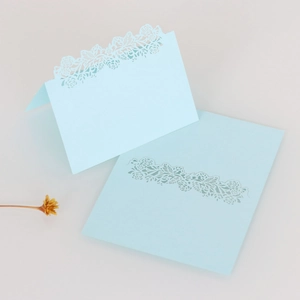 Detail of light blue laser-cut floral place card with intricate镂空leaf patterns