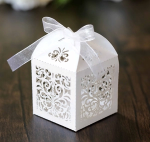 Close-up of laser-cut wedding favor box with floral patterns and a white organza ribbon