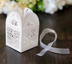 Macro shot of white laser-cut wedding candy box with vine patterns and sheer ribbon