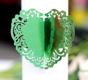 Detail of green metallic hollow heart napkin ring with laser cut vine patterns for weddings