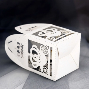 Detail of laser-cut white hollow carriage favor box with intricate floral wheel patterns