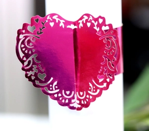 Macro shot of laser-cut heart napkin ring with metallic pink hollow floral patterns