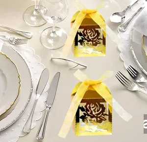 Close-up of golden laser-cut rose hollow favor boxes with yellow organza ribbons on table