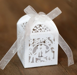 Close-up of laser-cut white wedding favor box with romantic couple silhouette and ribbon