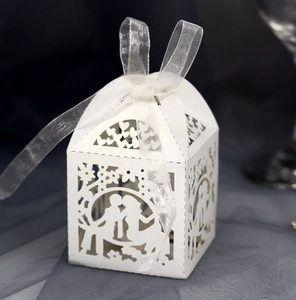 Macro shot of white laser-cut wedding candy box with couple motif and ribbon bow
