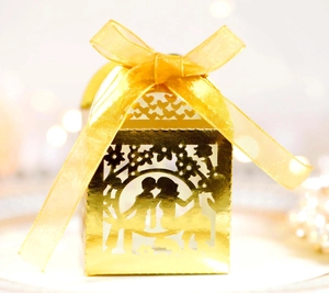 Detail of laser-cut gold wedding favor box with ribbon and romantic silhouette
