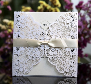 Detail of laser cut lace wedding invitation with white floral sleeve and cream ribbon bow