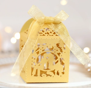Detail of laser-cut gold wedding favor box with romantic silhouette and organza ribbon bow