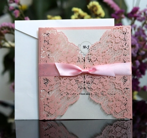 Detailed view of pink laser-cut lace wedding invitation with a silk ribbon bow