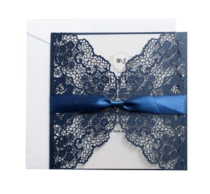 Navy blue laser cut wedding invitation with intricate lace patterns and a silk ribbon bow
