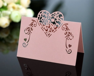 Detail of pink laser-cut wedding place card with intricate heart shape and lace patterns
