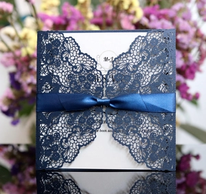 Detailed laser-cut flower patterns on navy blue wedding invitation with silk ribbon bow
