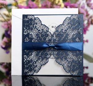 Close-up of laser-cut navy lace wedding invitation with a satin ribbon bow detail