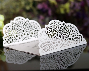 Elegant white laser-cut wedding invitation card with intricate floral lace on a mirror base