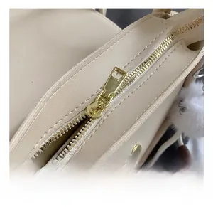 Detail of premium beige leather bag featuring gold hardware and a white plush pompom charm
