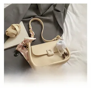 Detail view of off-white crossbody bag with red striped scarf and plush charm accessory
