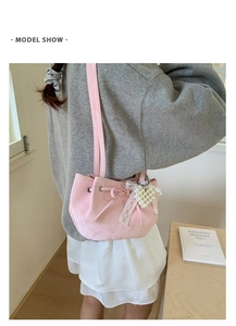 Detail of pink suede bucket bag with pearl heart charm and lace bow on a model