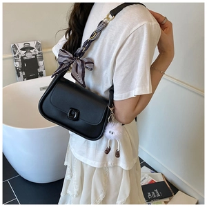 Detail of black crossbody bag featuring a silk ribbon strap and plush monster charm