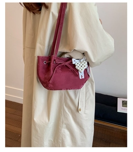 Detail of burgundy suede shoulder bag with drawstring bow and lace pearl heart charm