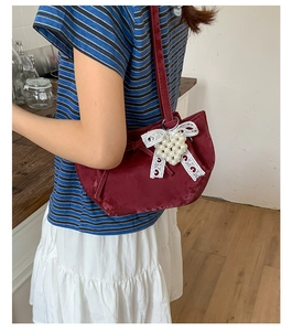 Detail of burgundy velvet underarm bag featuring a white lace bow and a pearl heart charm
