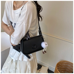 Detail showing black crossbody bag with flap buckle and plush monster charm attachment