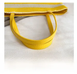 Detalle de asas de cuero amarillo con doble costura en un bolso tote de punto trenzado