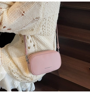 Detail of pink pebbled leather crossbody bag with silver hardware on a wooden staircase
