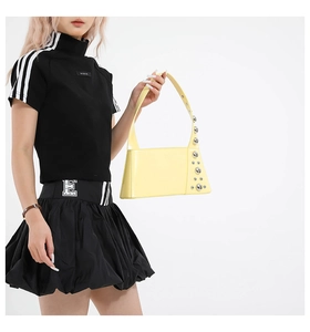 Detail shot of pale yellow trapezoid shoulder bag with silver metallic rivets on the side