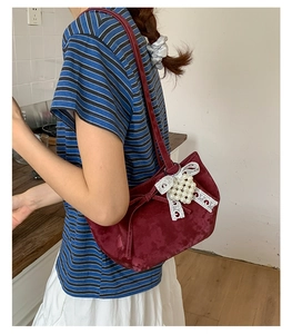Detail view of burgundy velvet shoulder bag with lace bow and pearl pendant on model