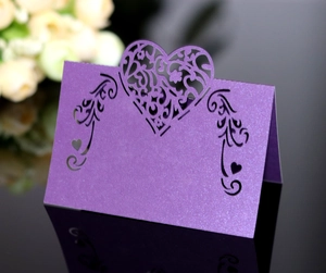 Macro shot of purple laser-cut wedding place card with heart patterns and pearlescent finish