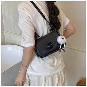 Detail of a black square flap crossbody bag featuring a cute white plush doll charm