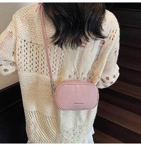 Sac bandoulière rose avec texture grainée et logo de marque porté sur un pull en maille beige
