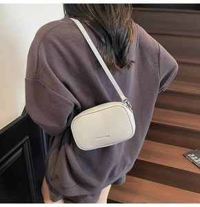 Vue détaillée d'un sac bandoulière en cuir gris porté par un mannequin dans un escalier